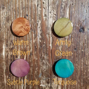 May include: Four round wooden discs, each painted a different color. The colors are warm brown, army green, subtle purple, and turquoise. The discs are labeled with their color names.
