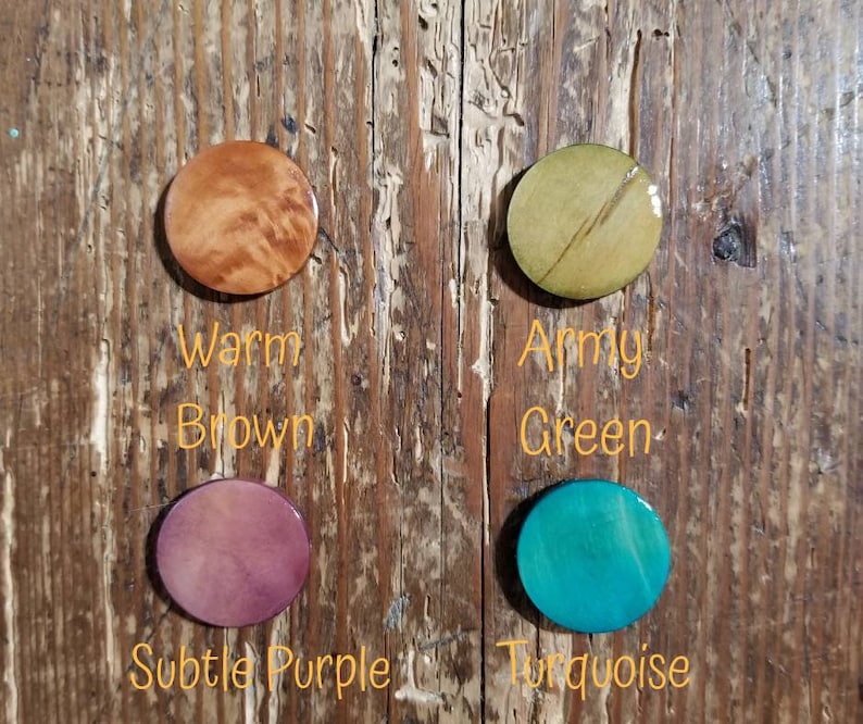 May include: Four round wooden discs, each painted a different color. The colors are warm brown, army green, subtle purple, and turquoise. The discs are labeled with their color names.