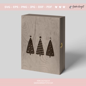 May include: Three Christmas trees with different patterns are carved into a wooden box. The trees are stylized and have a star, heart, and dots as their ornaments.