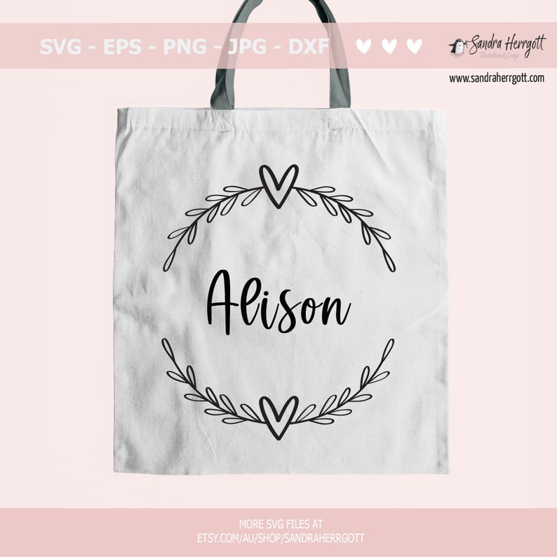 May include: A white tote bag featuring a black design of a wreath with leaves and hearts, and the name "Alison" in the centre.
