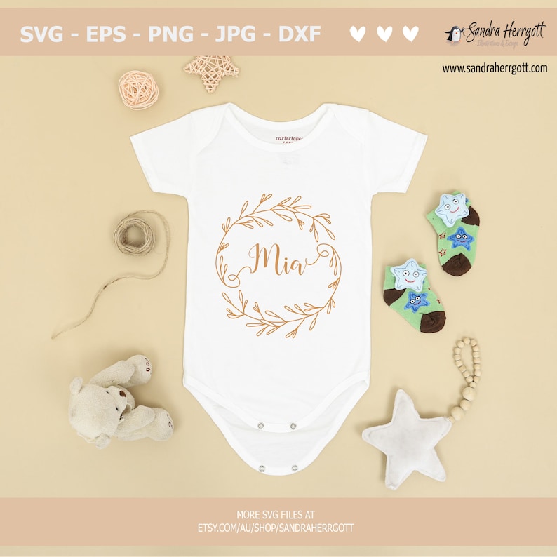 May include: A white baby onesie with a gold floral wreath and the name "Mia" in a cursive font.