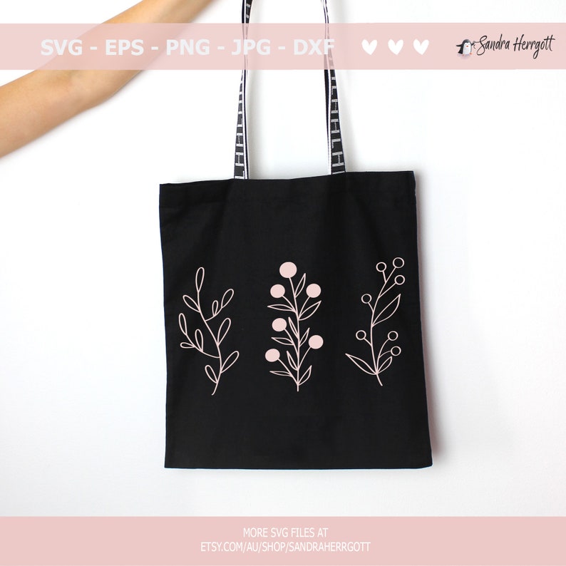 May include: A black tote bag with white straps and three pink floral designs on the front. The floral designs are simple line drawings of branches with leaves and berries.