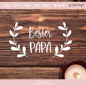 May include: White text on a wood background reads "Bester Papa" with a wreath of leaves around the text.