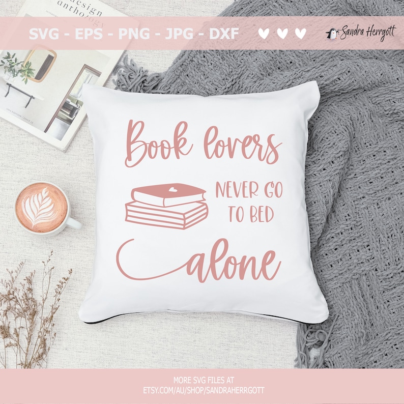 以下が含まれることがあります： ピンクの文字で「Book lovers never go to bed alone」と書かれた白い枕。文字は筆記体。ピンクの3冊の本が積み重ねられており、一番上の本には小さなハートマークが描かれている。枕は灰色の毛布の上に置かれている。