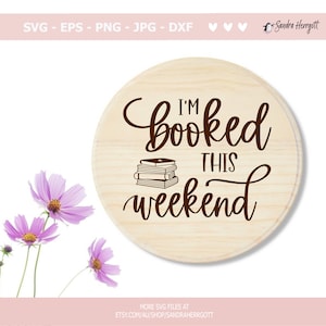 以下が含まれることがあります： 「I'm booked this weekend」という茶色の筆記体で書かれた丸い木製の看板。テキストの下には、一番上の本にハートが描かれた本の束が描かれている。
