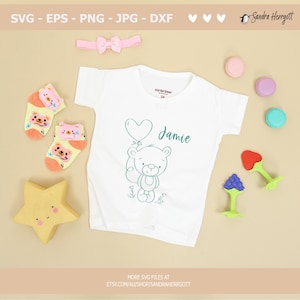 May include: A white baby onesie with a teal outline of a teddy bear holding a heart-shaped balloon. The onesie has the name "Jamie" written in teal script.