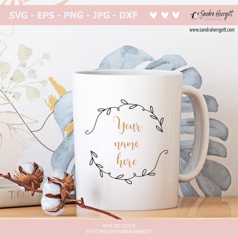 May include: White ceramic mug with a black outline of a floral wreath and the text "Your name here" in gold lettering.
