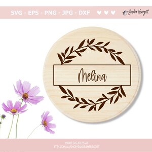 May include: A round wooden sign with a brown leafy wreath and a rectangular nameplate that says "Melina".