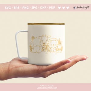 May include: A white mug with a gold outline of an elephant, giraffe, lion, and a smaller animal. The animals are surrounded by leaves and are sitting on a white background.