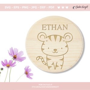 May include: A round wooden plaque with the name "ETHAN" engraved on it. A cartoon tiger with black stripes is also engraved on the plaque.
