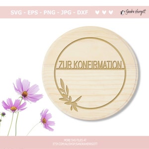 Peut inclure: Un cercle en bois avec un motif floral d&eacute;coratif et le texte "ZUR KONFIRMATION" en cercle autour du motif floral.