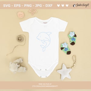 May include: A white baby onesie with a blue outline of a dolphin on the front. The onesie is surrounded by various baby items, including a star-shaped rattle, a pair of socks with stars, and a teddy bear.