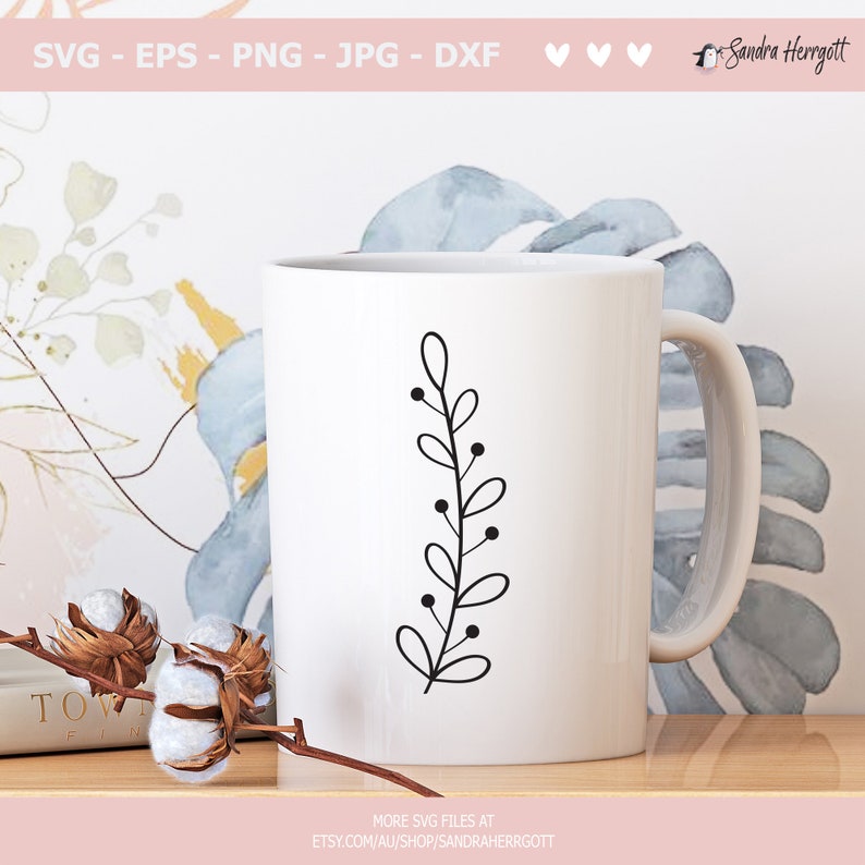 May include: A white ceramic mug with a black line drawing of a simple branch with leaves and berries. The mug is on a wooden surface.
