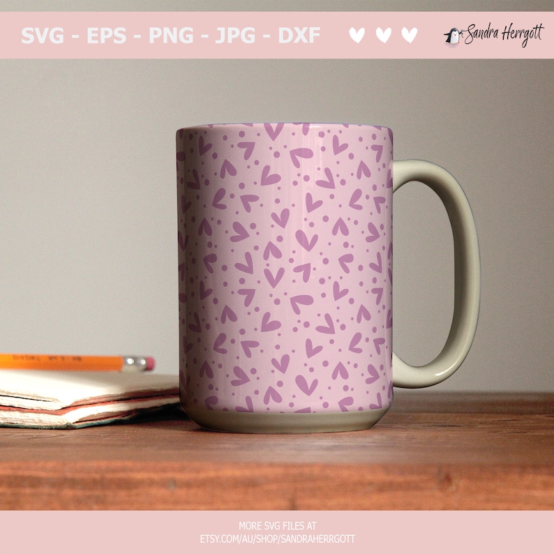 May include: A white ceramic mug with a handle. The mug has a pink background with a pattern of purple hearts and dots.
