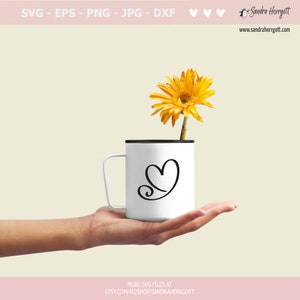 May include: A white mug with a black rim and handle, featuring a stylized heart design. A single yellow gerbera daisy is placed inside the mug.
