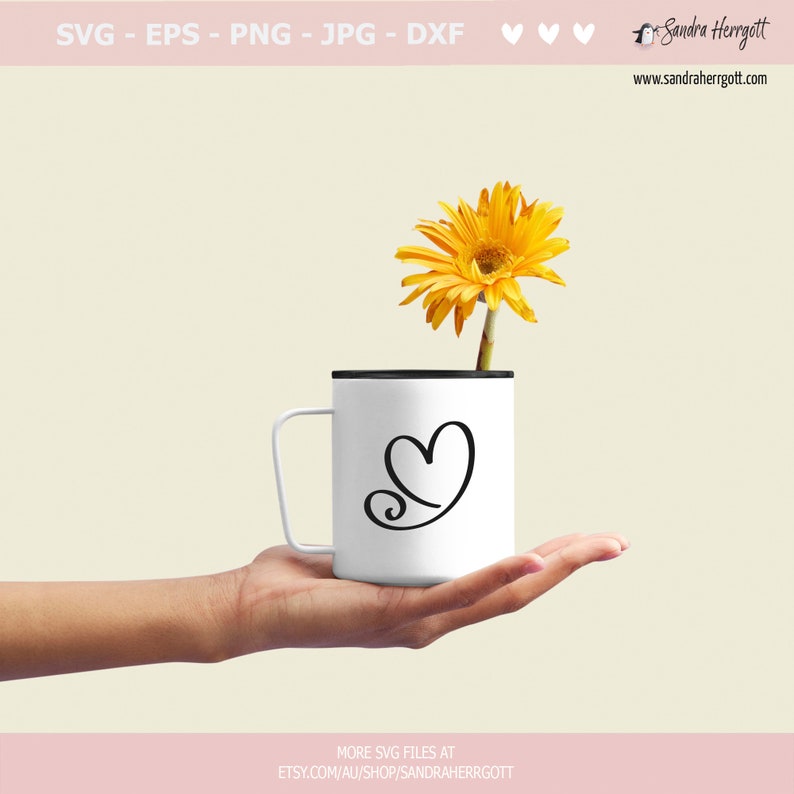 May include: A white mug with a black rim and handle, featuring a stylized heart design. A single yellow gerbera daisy is placed inside the mug.