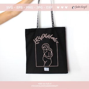 Pu&ograve; includere: Una borsa tote nera con un contorno rosa di una donna incinta in piedi in un arco floreale. Il testo "MORE SVG FILES AT ETSY.COM/AU/SHOP/SANDRAHERRGOTT" &egrave; stampato sul fondo della borsa.