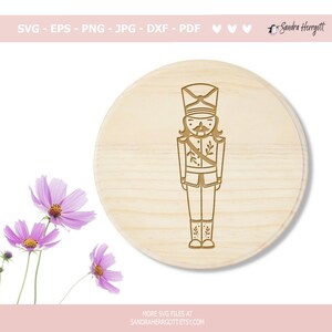 Może przedstawiać: Cyfrowy projekt żołnierza-łamacza orzech&oacute;w ze złotym obramowaniem na jasnobrązowym drewnianym tle.