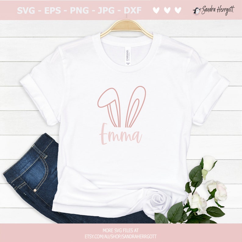 May include: White t-shirt with a pink bunny ears graphic and the name "Emma" in a matching font. The shirt is displayed with blue jeans and flowers, suggesting a spring or Easter theme. The top includes the text "SVG - EPS - PNG - JPG - DXF".