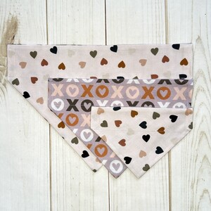 May include: Three fabric dog collars with a pink, brown, and black heart pattern. The collars are layered on top of each other, with the largest collar at the bottom and the smallest collar at the top.