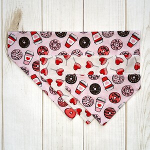 May include: Pink and white dog bandana with a pattern of donuts, coffee cups, and hearts. The bandana has a white border and the text "Love You" on it.