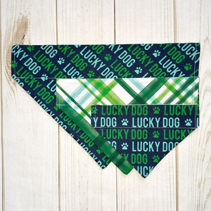 May include: A reversible dog bandana with a green and white plaid pattern on one side and a navy blue pattern with the text "Lucky Dog" repeated on the other side.