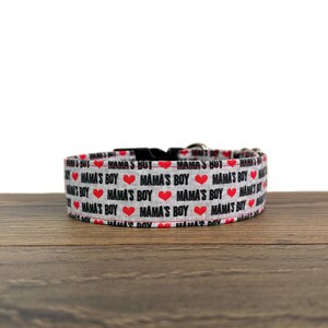 May include: A gray dog collar with a red heart and black text that reads "Mama's Boy" repeated on the collar.