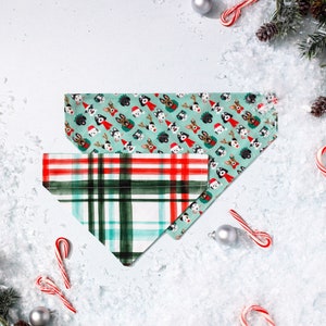 May include: Two dog-themed bandana collars. One is green with a plaid pattern and features cartoon dogs wearing Santa hats. The other is a red and green plaid pattern.