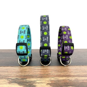 May include: Three dog collars with a repeating pattern of green tennis balls and the text "Ball is Life". The collars are in turquoise, gray, and purple.
