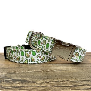 May include: Two avocado-patterned dog collars with silver buckles. The collars are on a wooden surface. The larger collar has the text "Chewy" on the buckle.