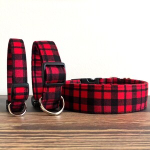May include: Three red and black plaid dog collars of different sizes. The collars have black metal D-rings and black plastic buckles.