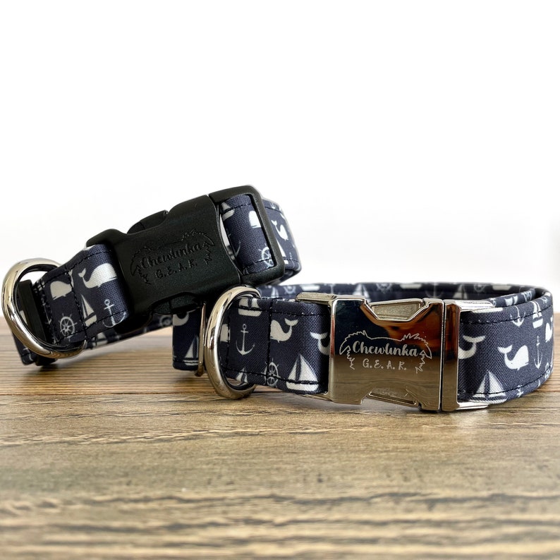 May include: Two navy blue dog collars with white whale, anchor, and sailboat designs. The collars have silver buckles with the text "Chewlnka G.E.A.R." engraved on them.