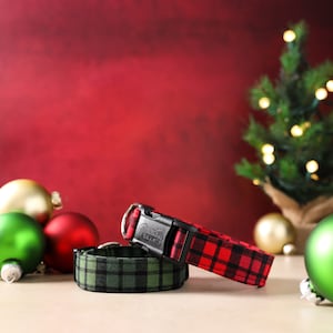 May include: Two dog collars with plaid patterns. One collar is red and black plaid, the other is green and black plaid. Both collars have black buckles.