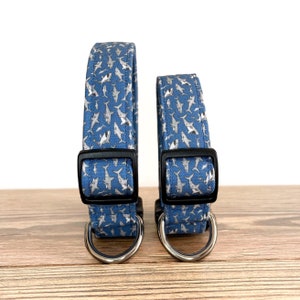 May include: Two dog collars with a blue background and a silver shark pattern. The collars have black buckles and silver D-rings.