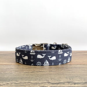 May include: A navy blue dog collar with a white whale, sailboat, anchor, and steering wheel pattern.