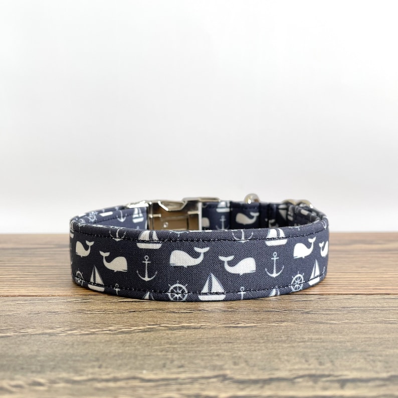 May include: A navy blue dog collar with a white whale, sailboat, anchor, and steering wheel pattern.