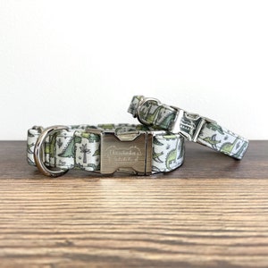 May include: Two dog collars with a green and white dinosaur print. The larger collar has a silver buckle with the text "Chewtinka's" engraved on it.