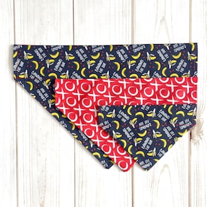 May include: Three dog bandanas with a blue background and a pattern of yellow bananas with the text "Bananas for you" and red hearts. The middle bandana is red with a white pattern of Xs and Os.