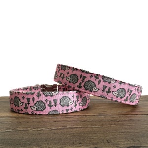 May include: Two pink dog collars with a hedgehog pattern. The collars are made of fabric and have a silver buckle.