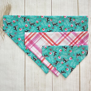 May include: Three dog bandanas, one with a pink and white plaid pattern, and two with a turquoise background and a repeating pattern of black and white skunks with the text "Love Stinks" and "Skulls & Stinks".