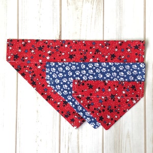 May include: A red, white, and blue dog bandana with a star pattern. The bandana is layered with a smaller blue bandana with a white paw print pattern.