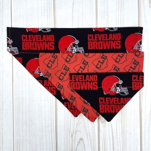 May include: Three different sizes of dog bandanas featuring the Cleveland Browns logo and team colors. The bandanas are black with orange and white accents. The largest bandana has the words "Cleveland Browns" printed on it. The medium bandana has the words "Cleveland Browns" printed on it. The smallest bandana has the words "Cleveland Browns" printed on it.
