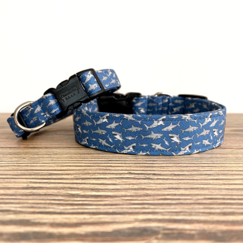 May include: Two blue dog collars with a white shark print. The collars have black buckles and silver D-rings.