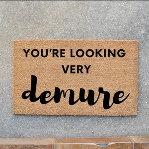 May include: A brown coir doormat with the text "You're looking very demure" in black lettering.