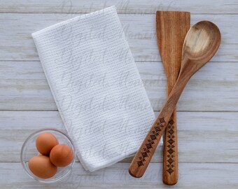 Puede incluir: Tres huevos marrones en un tazón de vidrio transparente, una toalla de cocina blanca y dos utensilios de cocina de madera con tallas decorativas sobre un fondo de madera blanca.