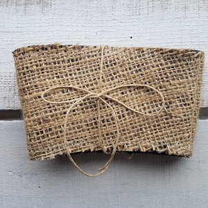 May include: A brown burlap coffee cup sleeve tied with twine. The sleeve is made of natural burlap fabric and has a rustic look.