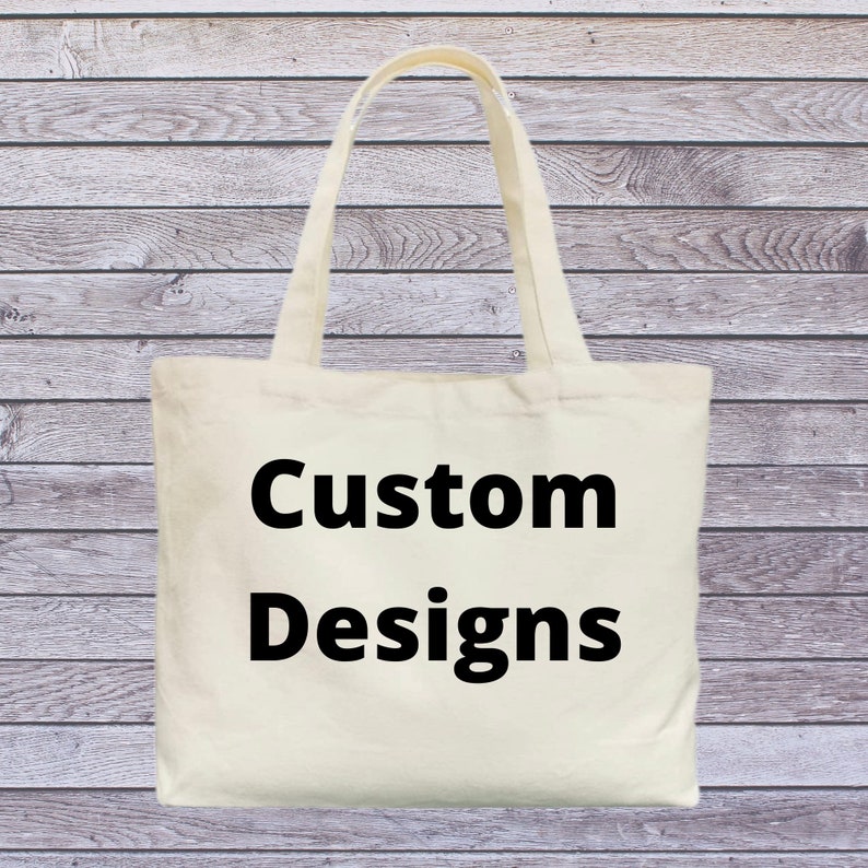 May include: A white canvas tote bag with black handles and the text "Custom Designs" printed in black.