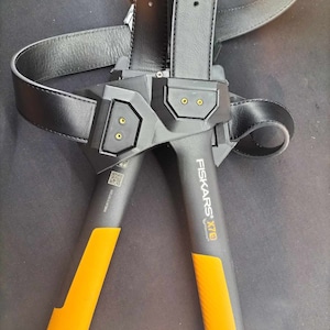 May include: A black leather belt with a black and orange axe attached. The axe has the text "Fiskars X7®" printed on the handle.