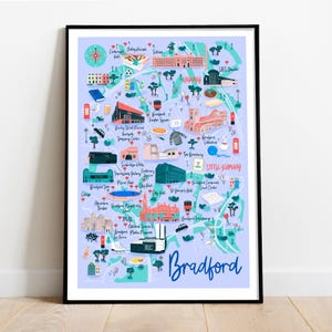 May include: A framed print of a map of Bradford, West Yorkshire, with illustrated landmarks and the city's name in a stylized font. The map is in shades of blue, with red and green accents, and includes text such as "Little Germany".