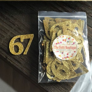 May include: Gold glitter number 67 with a bag of gold glitter confetti letters that say "The Fetti Boutique Balloons and Party Decor".